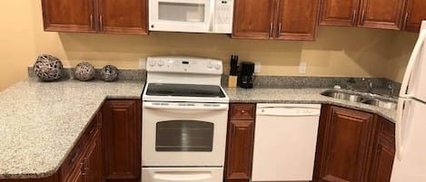 A kitchen with wooden cabinets, a microwave, a stove, a dishwasher, and a granite countertop.