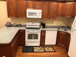 Una cocina con armarios de madera, microondas, estufa, lavavajillas y encimera de granito.