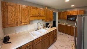 A kitchen with wooden cabinets, a white sink, a stainless steel refrigerator, and a microwave.