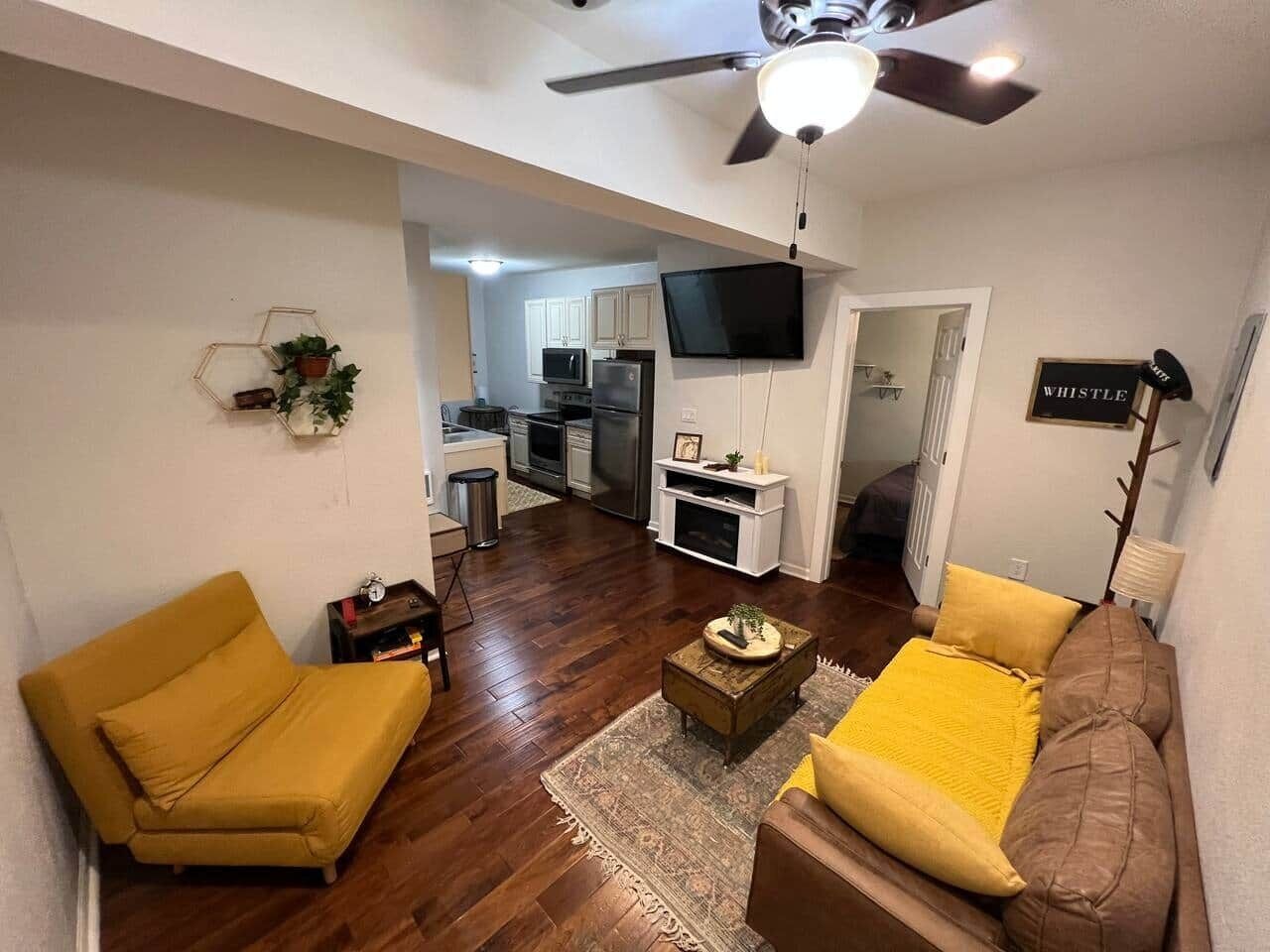 Ein Wohnzimmer mit Sofa, Couchtisch und Fernseher. Im Hintergrund ist eine Küche zu sehen.
