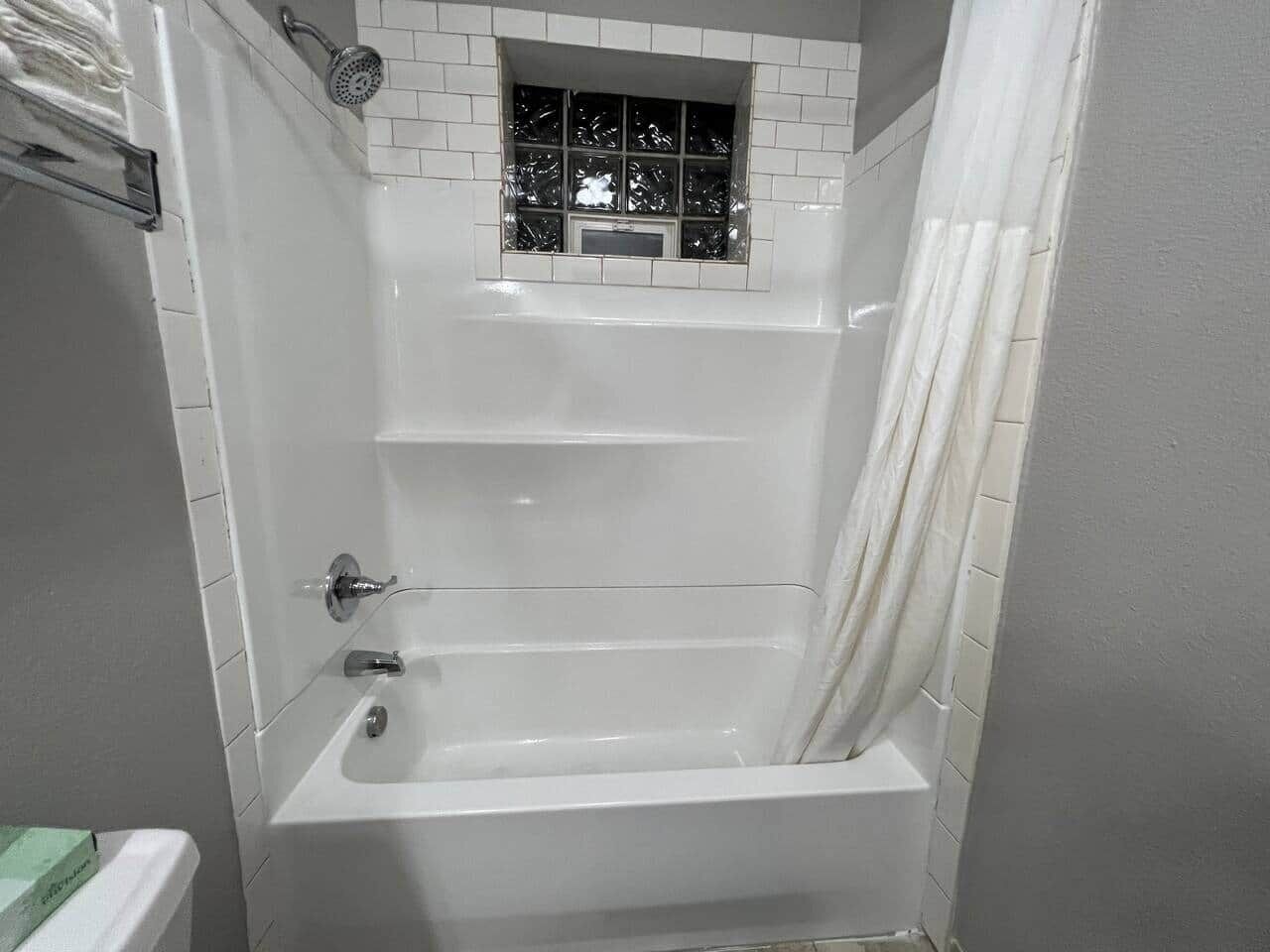 Ein Badezimmer mit einer Badewanne, einer Duschbrause, einem Fenster und einem Vorhang.