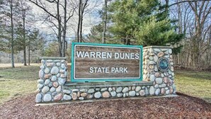 En skylt för Warren Dunes State Park, med en stenmur och en logotyp.