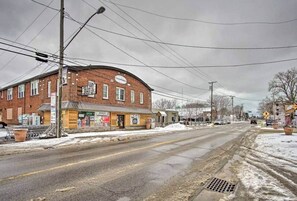 A brick building with a storefront, a pedestrian crossing sign, and a street with snow. - Beach Town Retreat | 2BR Near Dunes and Downtown (Shorewood-Tower Hills-Harbert)