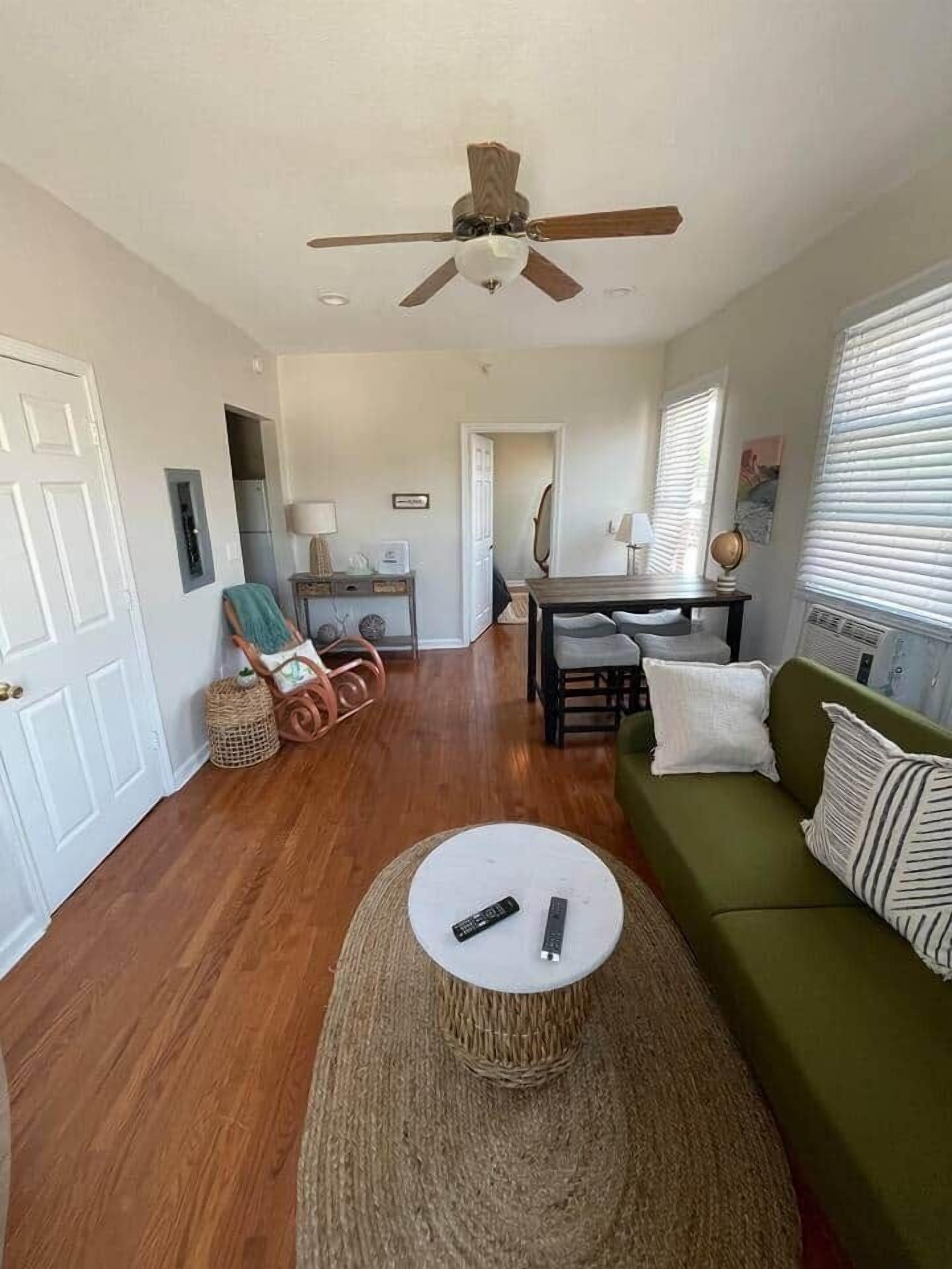 A living room with a ceiling fan, a green sofa, a round coffee table, and a dining area with a table and chairs.