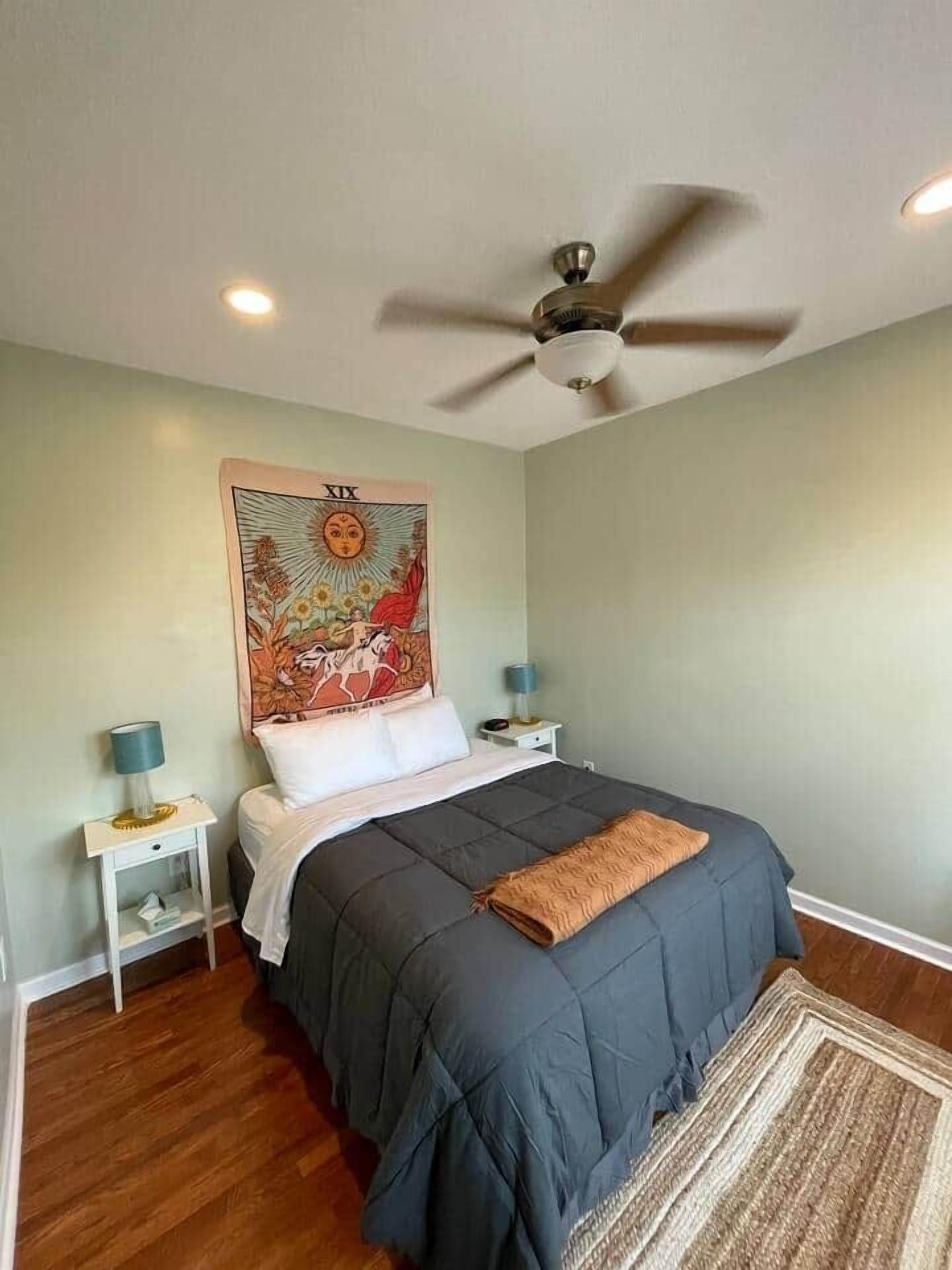Une chambre à coucher avec un lit, un ventilateur de plafond, une tapisserie murale, des tables de chevet et un tapis.