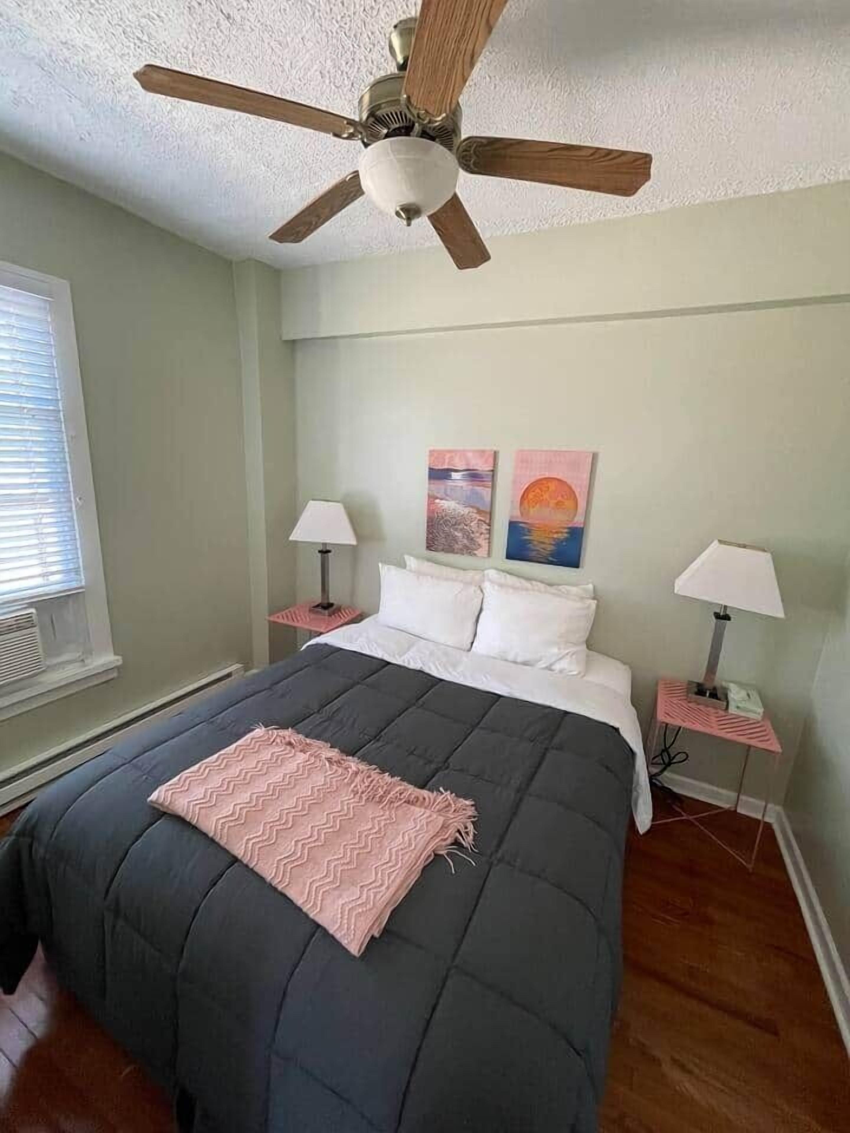 Un dormitorio con una cama, dos mesitas de noche, un ventilador de techo y cuadros en la pared.