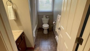 A narrow hallway leading to a bathroom with a toilet, a towel rack, and a small window.