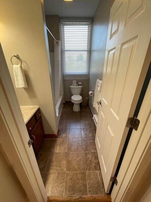 A narrow hallway leading to a bathroom with a toilet, a towel rack, and a small window. - Beach Town Retreat | 2BR Near Dunes and Downtown (Shorewood-Tower Hills-Harbert)