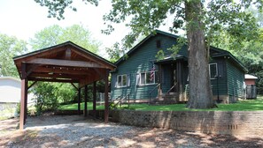 A two-story house with a porch and a covered area, surrounded by trees.