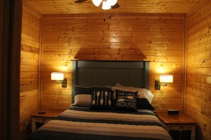 A wooden cabin-style bedroom with a bed, two bedside lamps, and a ceiling fan.