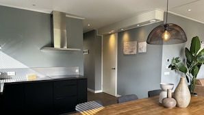A modern kitchen with a wooden dining table, a hanging light fixture, and a plant on the table. - Holiday Home in Lochem With Terrace (Lochem)