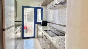A modern kitchen with a built-in stove, stainless steel cabinets, and a large window with blinds. - Terrasol Costaluz Torre del Mar (Torre del Mar)