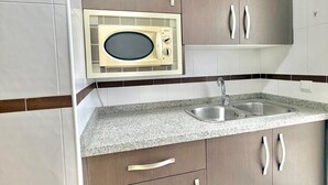 A kitchen with a microwave, double sink, and wooden cabinets. - Terrasol Costaluz Torre del Mar (Torre del Mar)