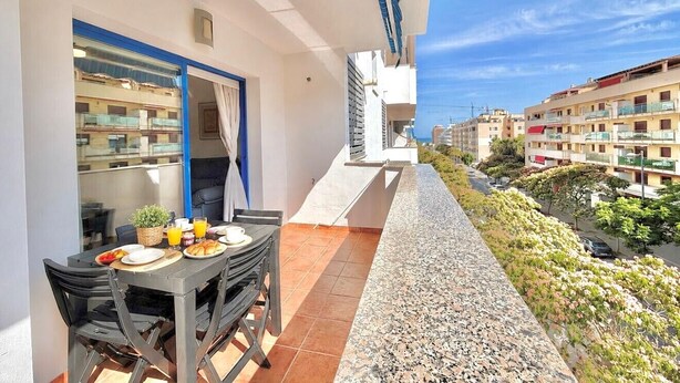 A balcony with a table set for breakfast, a door leading to a room, and a view of the street and buildings. - Terrasol Costaluz Torre del Mar (Torre del Mar)