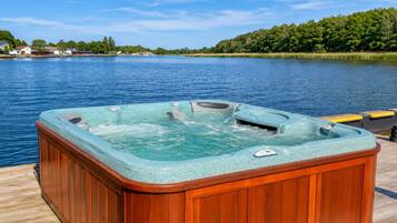 A hot tub on a wooden deck by a lake with a clear sky.