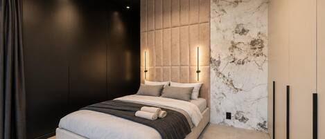 A modern bedroom with a bed, a headboard with built-in lighting, and a marble-patterned wall.