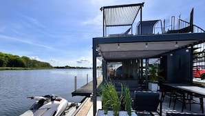 A modern dock with a seating area, a boat, and a view of the water. - Comfortable Dziwnow House for 8 (Dziwnów)