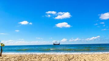 A beach with a boat in the distance, clear skies, and calm sea.