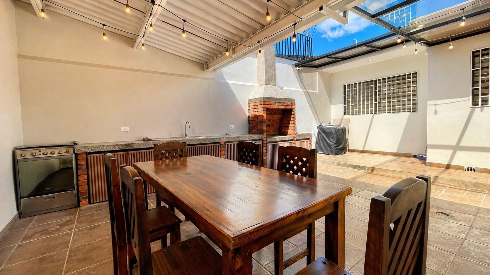 Een terras buiten met een houten tafel en stoelen, een bakoven en een keuken met een fornuis.
