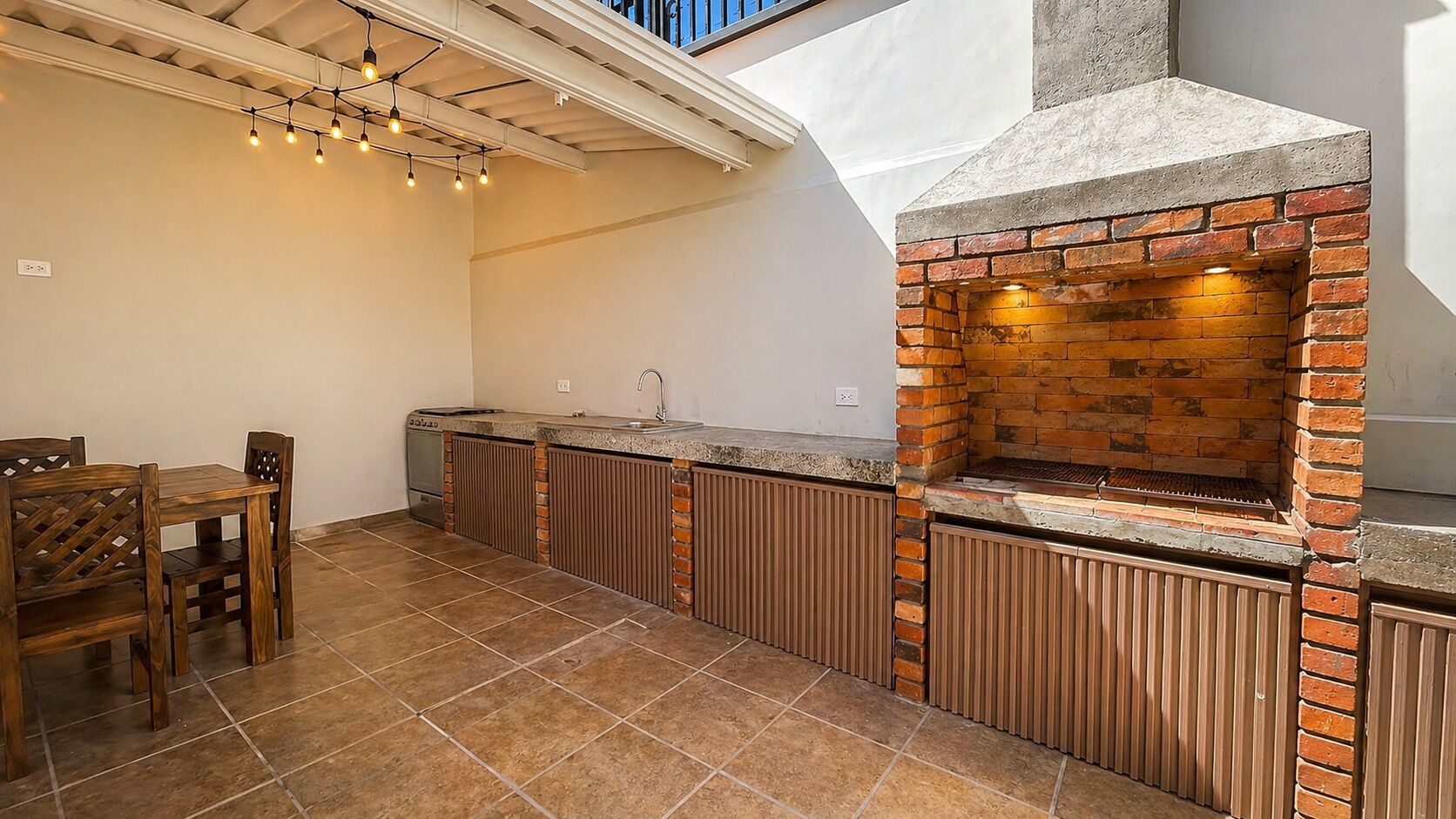 An outdoor kitchen with a brick oven, a dining area with chairs, and a ceiling light fixture.
