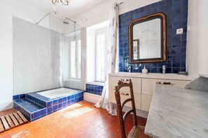 Une salle de bain avec une douche en verre, une baignoire, un lavabo avec un miroir et une chaise en bois.