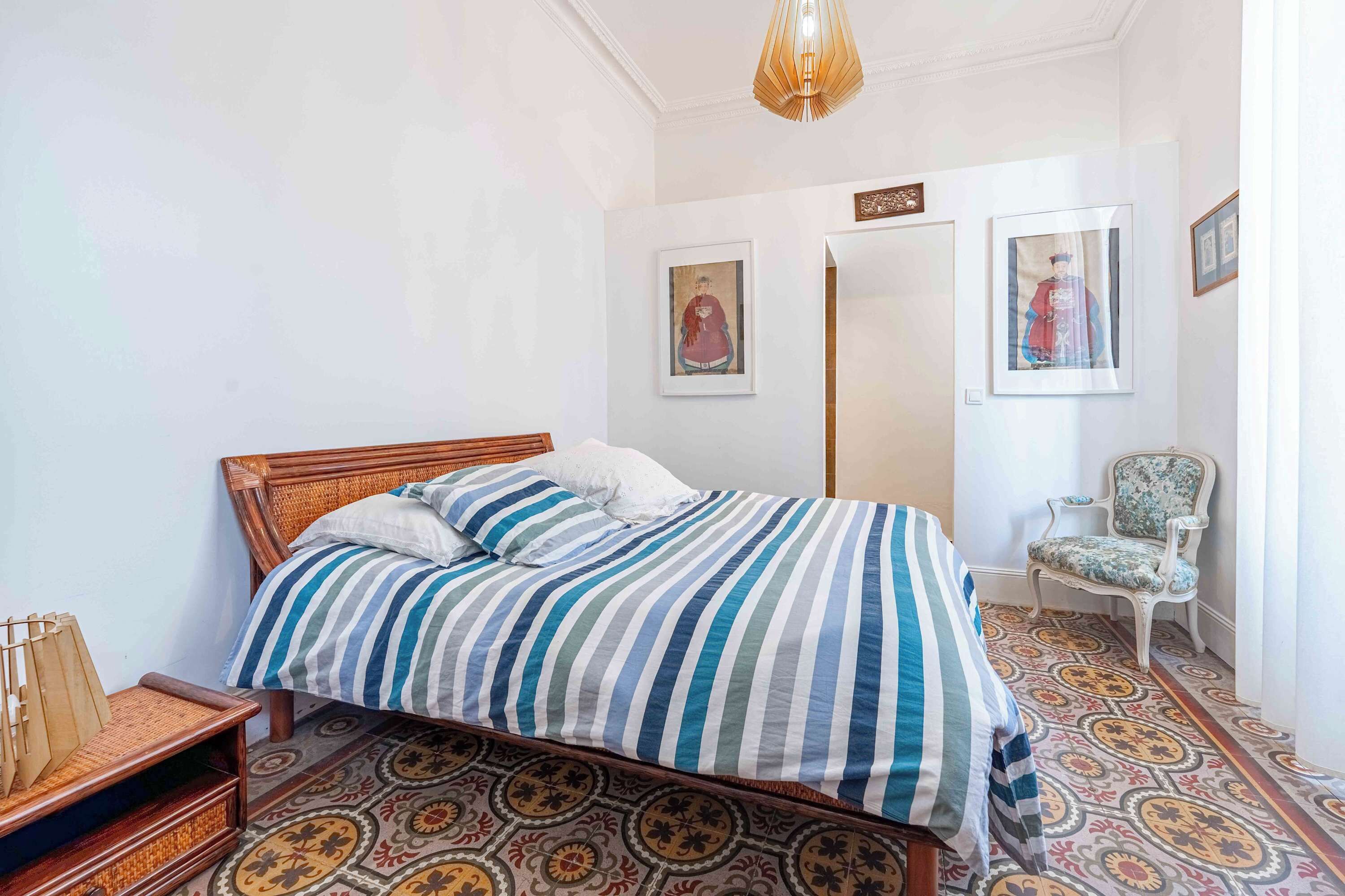 A bedroom with a wooden bed, striped bedding, a patterned floor, and two framed pictures on the wall.