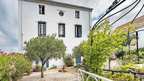 Un edificio blanco con tres ventanas, una puerta y un jardín con plantas y una maceta.