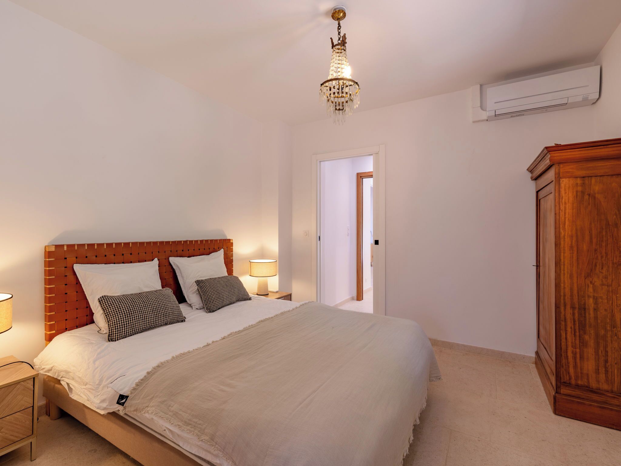 Ein Schlafzimmer mit hölzernem Kopfteil, einem Bett mit weißen Bettwäsche, einer Chandelieber, einer Klimaanlage und einem Holzschrank.