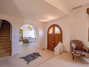 Ein geräumiger Wohnbereich mit einer Holztreppe, einem Zebra-Teppich, einer Holztür und einem gemusterten Sofa.