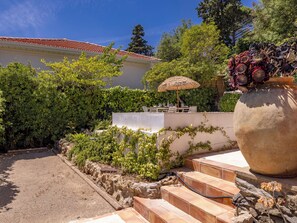 Eine Terrasse mit Tisch und Stühlen, eine große Vase mit Blumen und eine Mauer mit Kletterpflanzen.