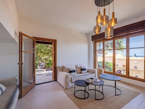 A room with a sofa, two small tables, a hanging light fixture, and a large window with a view. - Floralies by Interhome (Sainte Maxime)