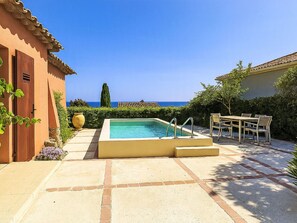 A pool area with a view of the sea, a dining table, and a building with a door. - Floralies by Interhome (Sainte Maxime)