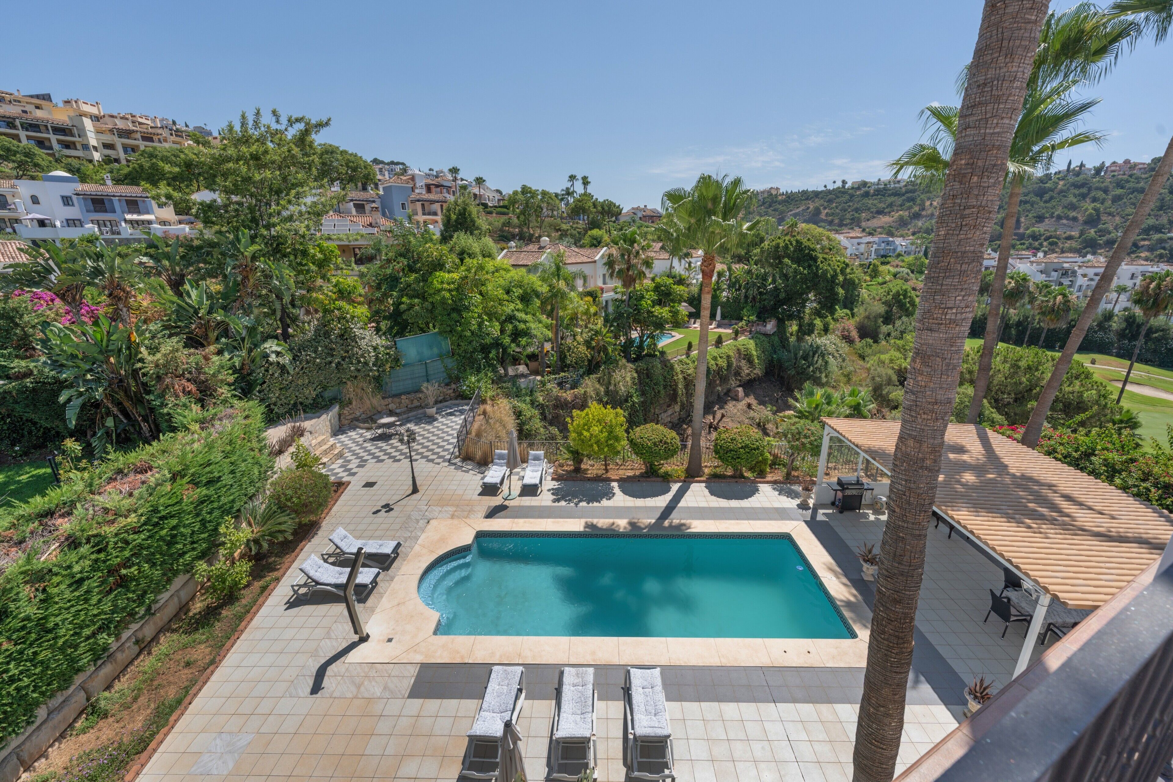 Un área de piscina con sillas de descanso, una zona de estar techada y vistas de edificios circundantes.