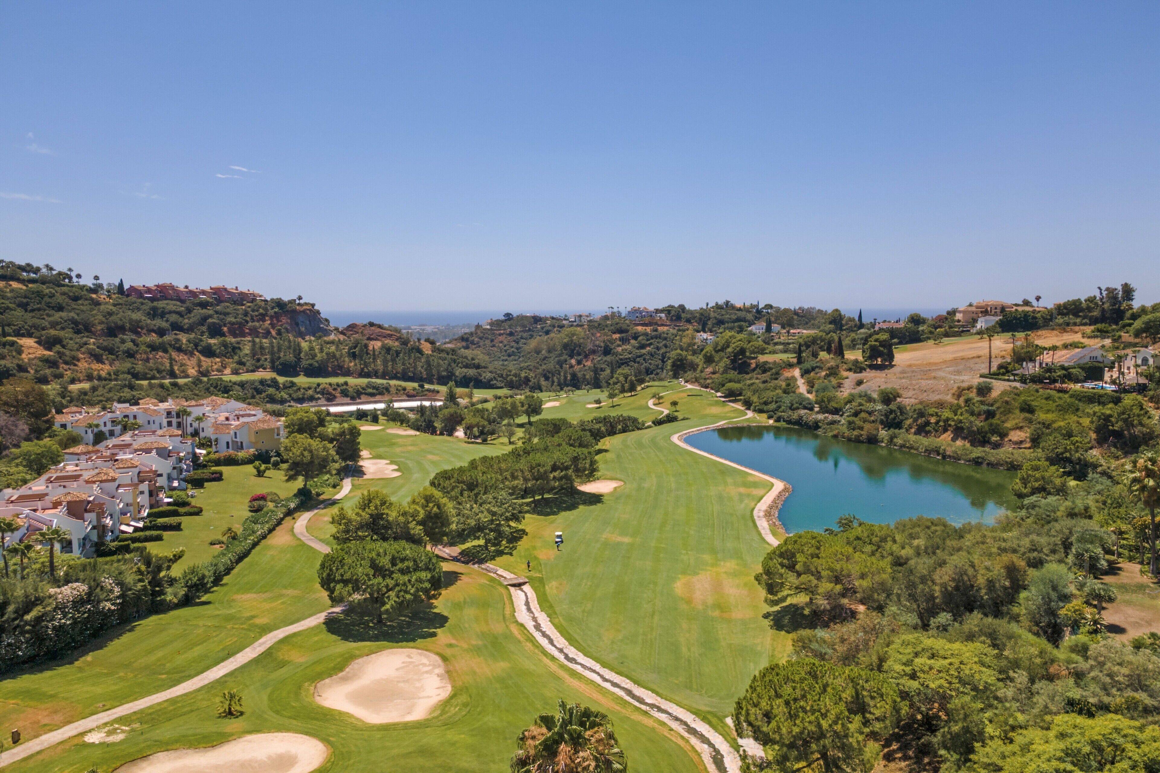 A golf course with a lake, surrounded by greenery and residential buildings.