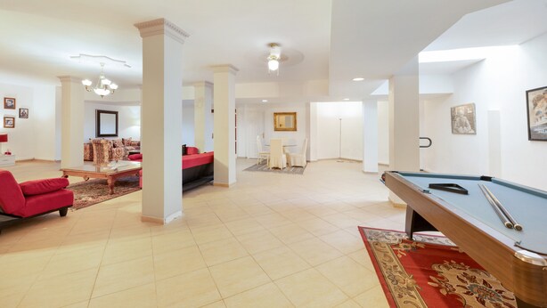 A spacious living area with a pool table, red sofas, and a dining area.