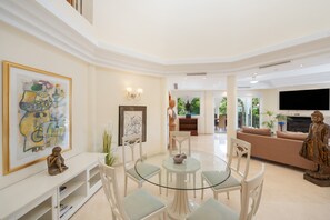 Un salón amplio con una mesa de vidrio, sillas blancas, un sofá y un televisor.