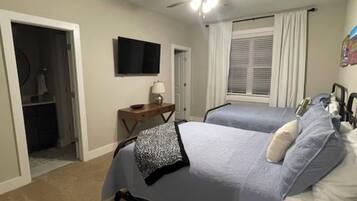A bedroom with two beds, a ceiling fan, a TV, and a desk with a lamp.
