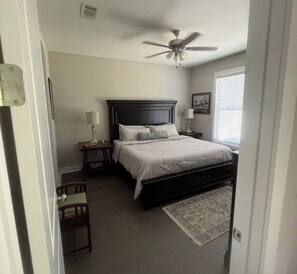 A bedroom with a bed, a nightstand, a chair, a ceiling fan, and a window with blinds.