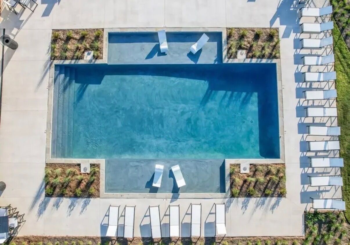 An aerial view of a rectangular swimming pool with two sets of white lounge chairs on opposite sides.