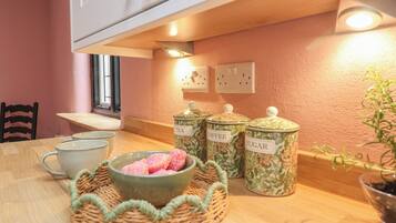 Una cocina con una mesa de madera, un cuenco con objetos rosas y tres recipientes etiquetados para té, café y azúcar.