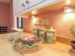 Une cuisine avec une table en bois, un bol rempli d’objets roses et trois récipients étiquetés pour le thé, le café et le sucre.