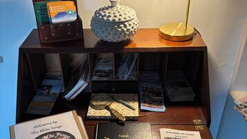 Una mesa de madera con varios objetos, incluyendo un libro titulado 'The Olde Forge', un 'Libro de visitas' y una lámpara.
