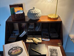 Une table d’exposition en bois sur laquelle sont disposés divers objets, notamment un livre intitulé « The Olde Forge », un « livre d’or » et une lampe.