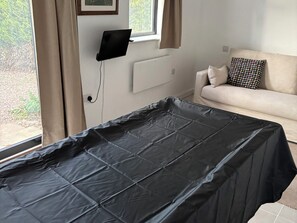 Ein Zimmer mit einem Bett, das mit einer schwarzen Bettdecke bezogen ist, einem Fenster mit Vorhängen, einem Sofa mit gemusterten Kissen und einem an der Wand montierten Fernseher.
