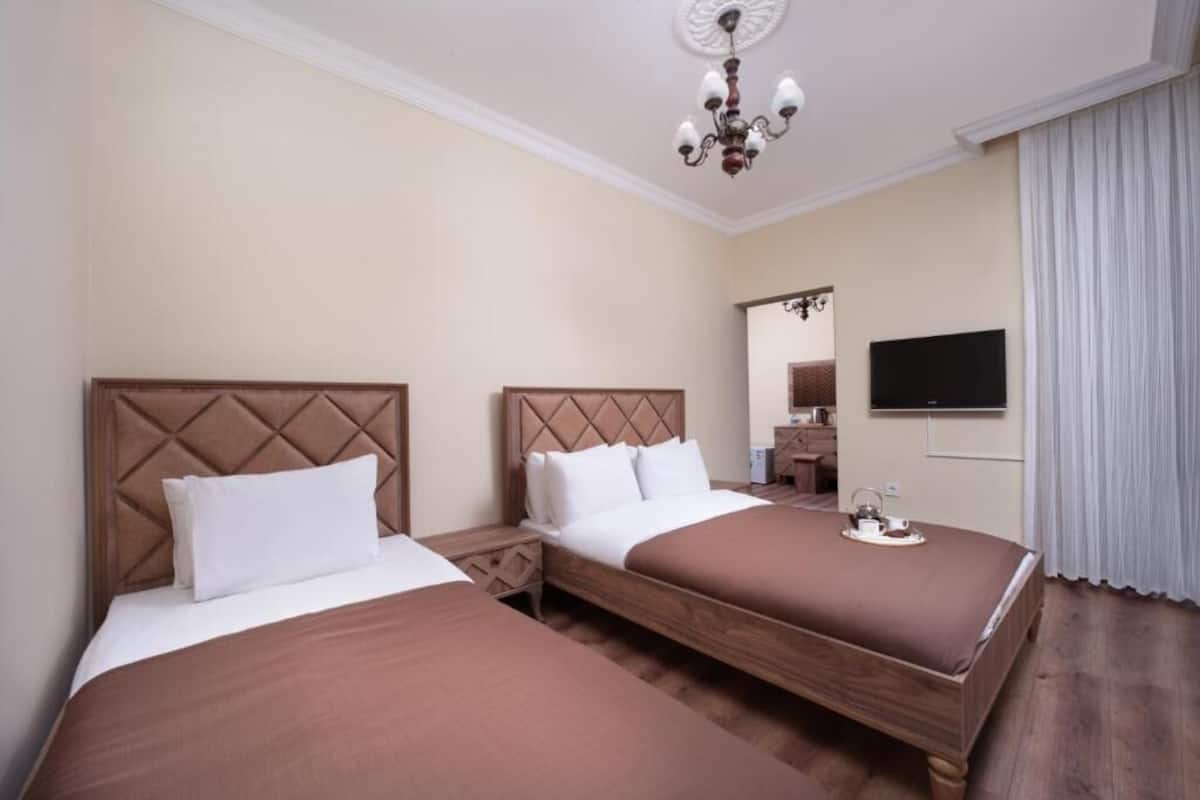 A hotel room with two beds, a television, a mirror, and a chandelier.