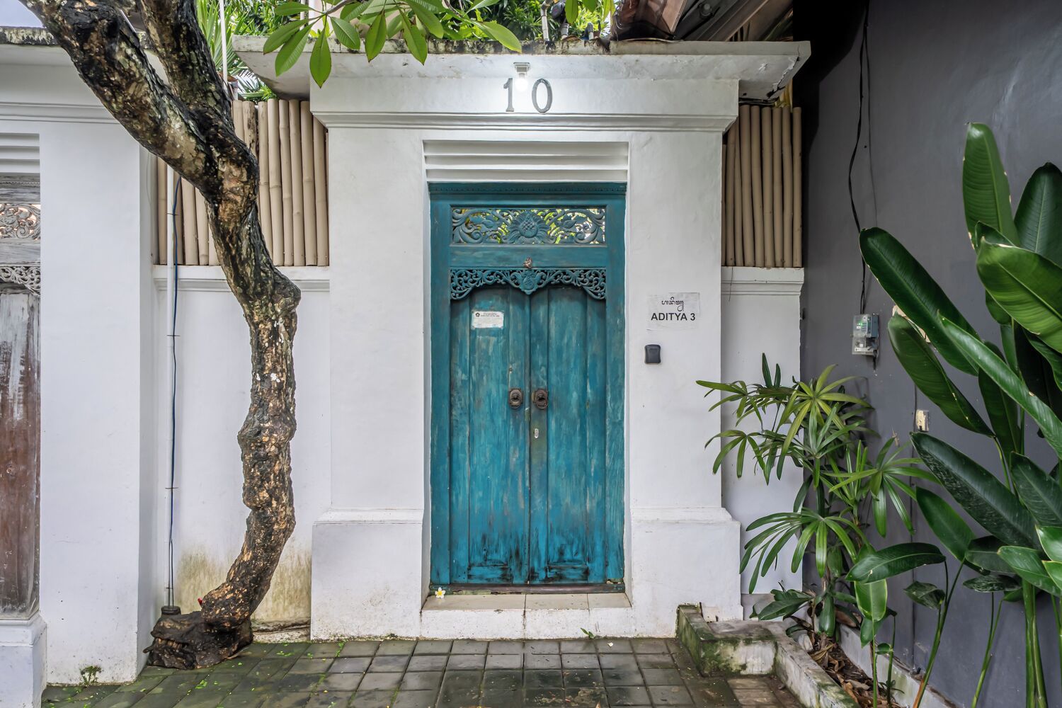 A teal door with a decorative top, a white wall with a number '10' above it, and a sign reading 'ADITYA 3'.