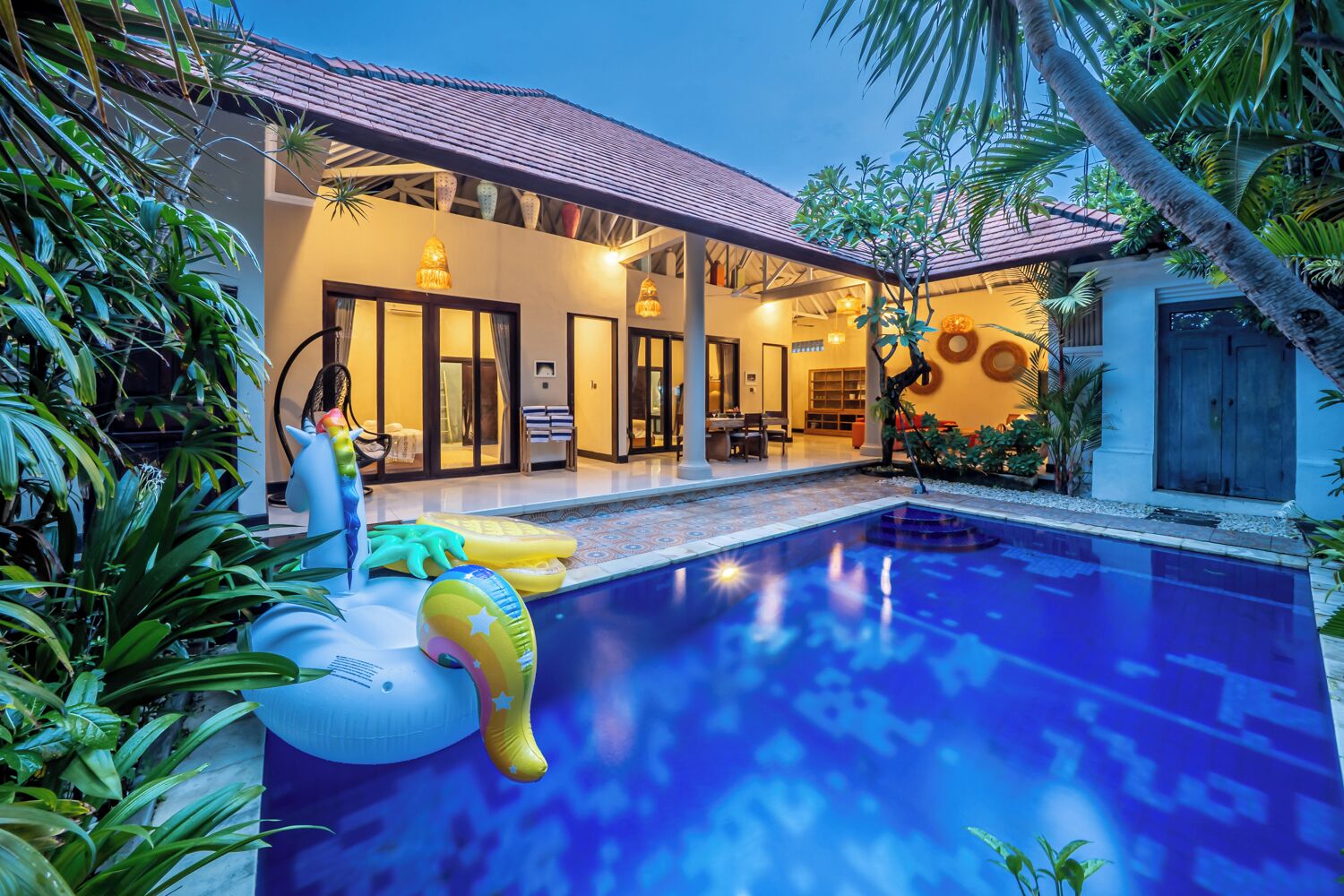 A swimming pool with inflatable toys, a covered patio, and lush greenery.