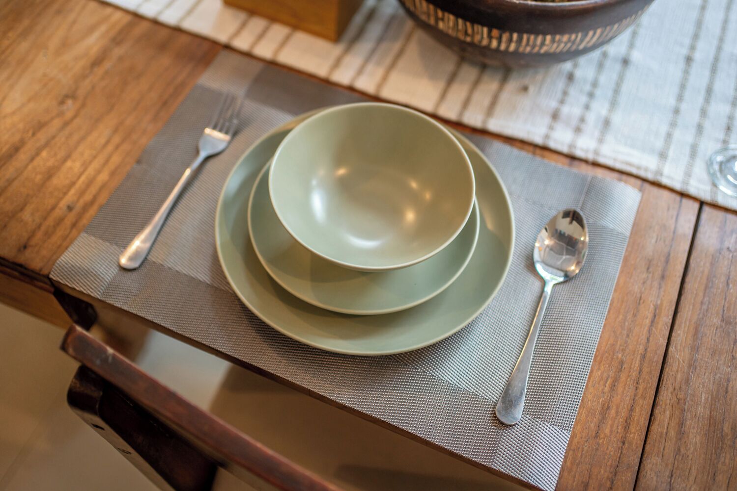 Una mesa con un mantel individual, un cuenco verde, una cuchara y un tenedor.