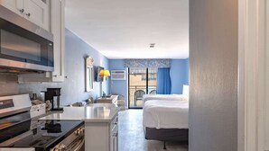 Ett kompakt hotellrum med ett litet pentry, en säng, ett litet bord och ett fönster med utsikt.