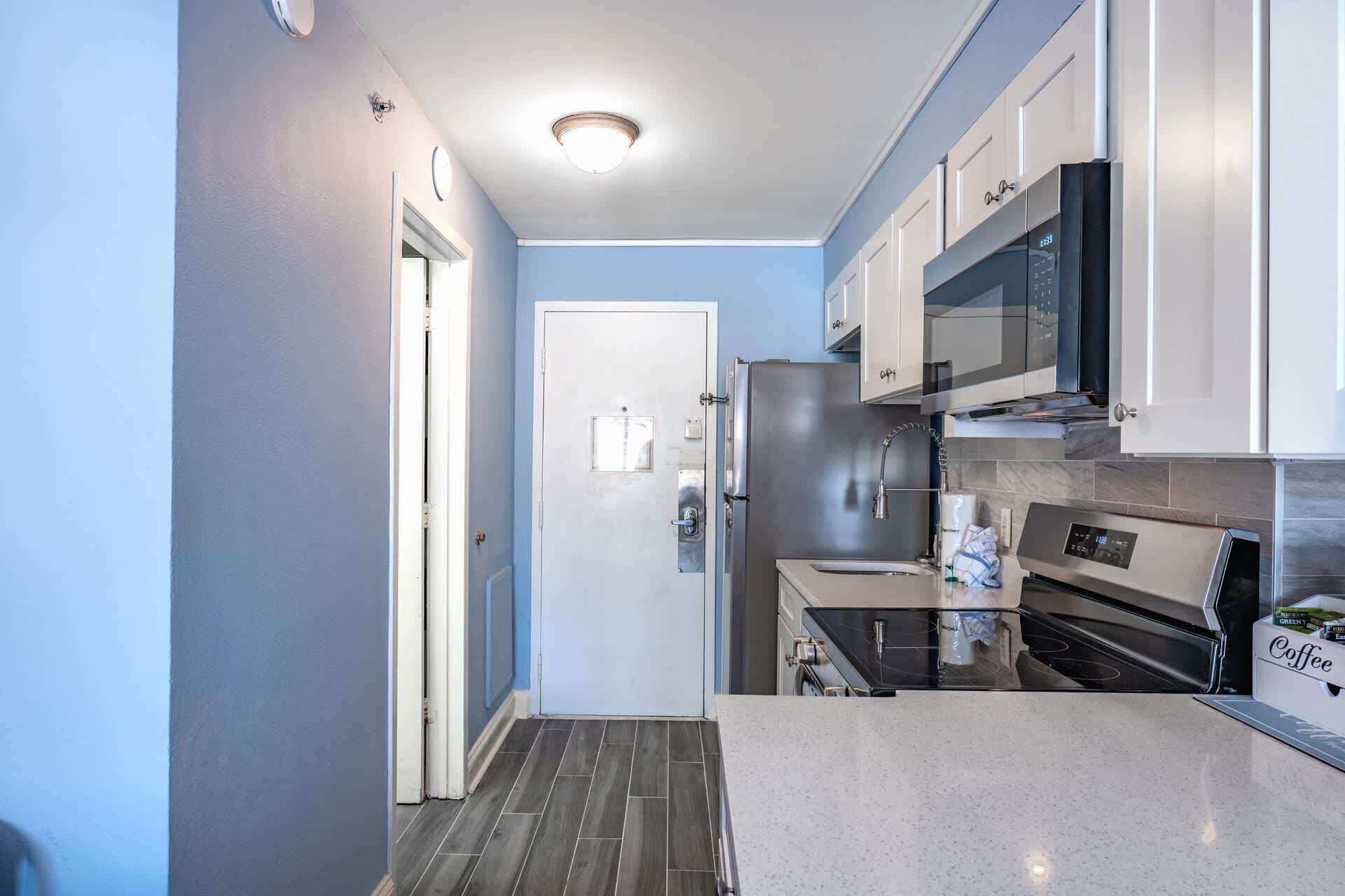 A compact kitchen with a refrigerator, microwave, oven, and a coffee station.